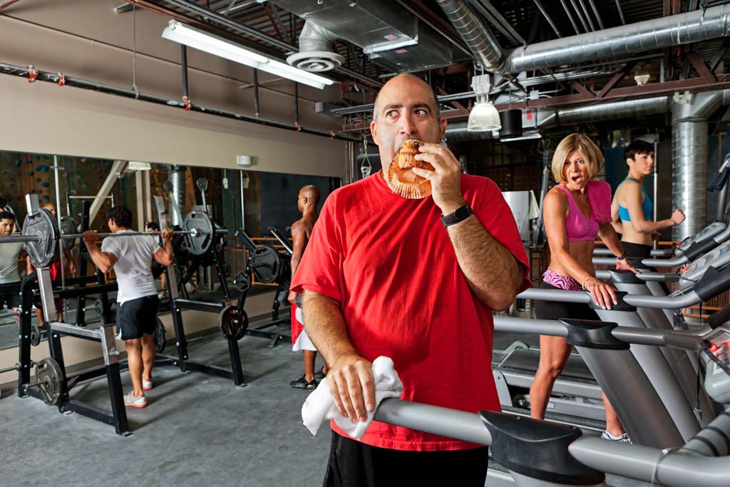 A man eats a muffin on a treadmill, shocking other gym patrons.