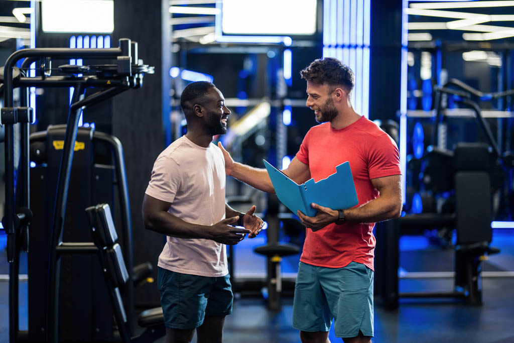 A personal trainer consults with a client in a gym.