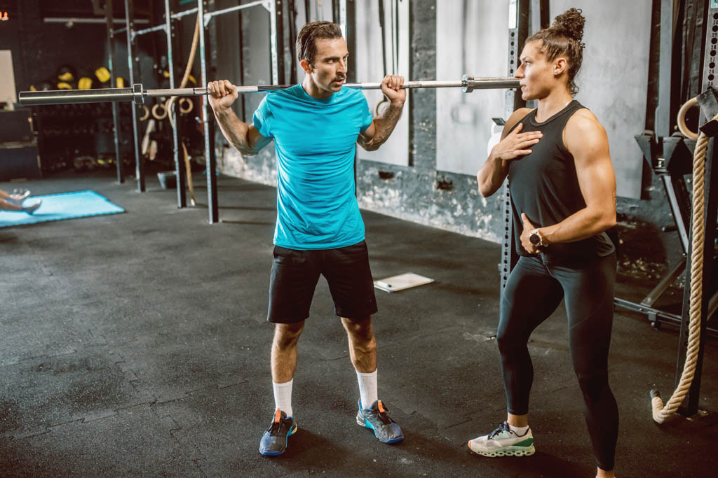 A CrossFit affiliate owner teaches an athlete to squat during a personal training session.