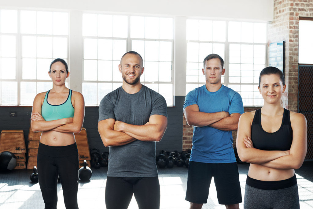 A group of 4 people standing in a gym. Two are smiling and two are not.