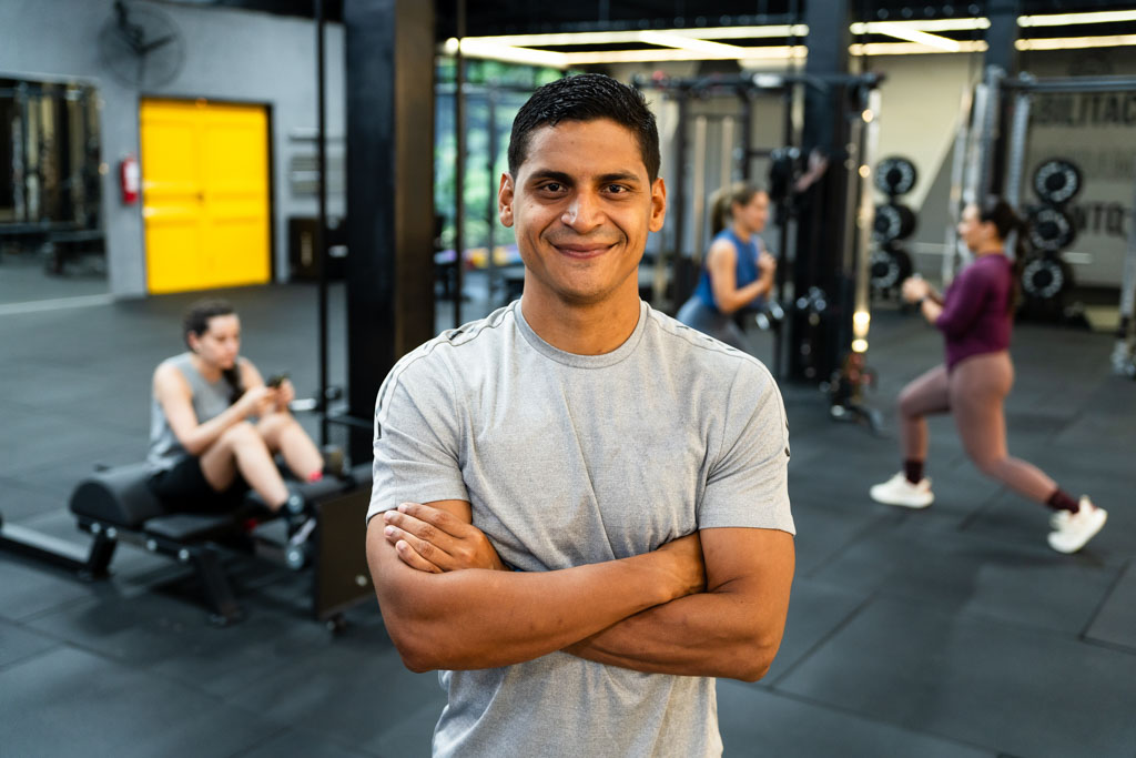 A confident, smiling gym owner stands with arms crossed on his training floor.