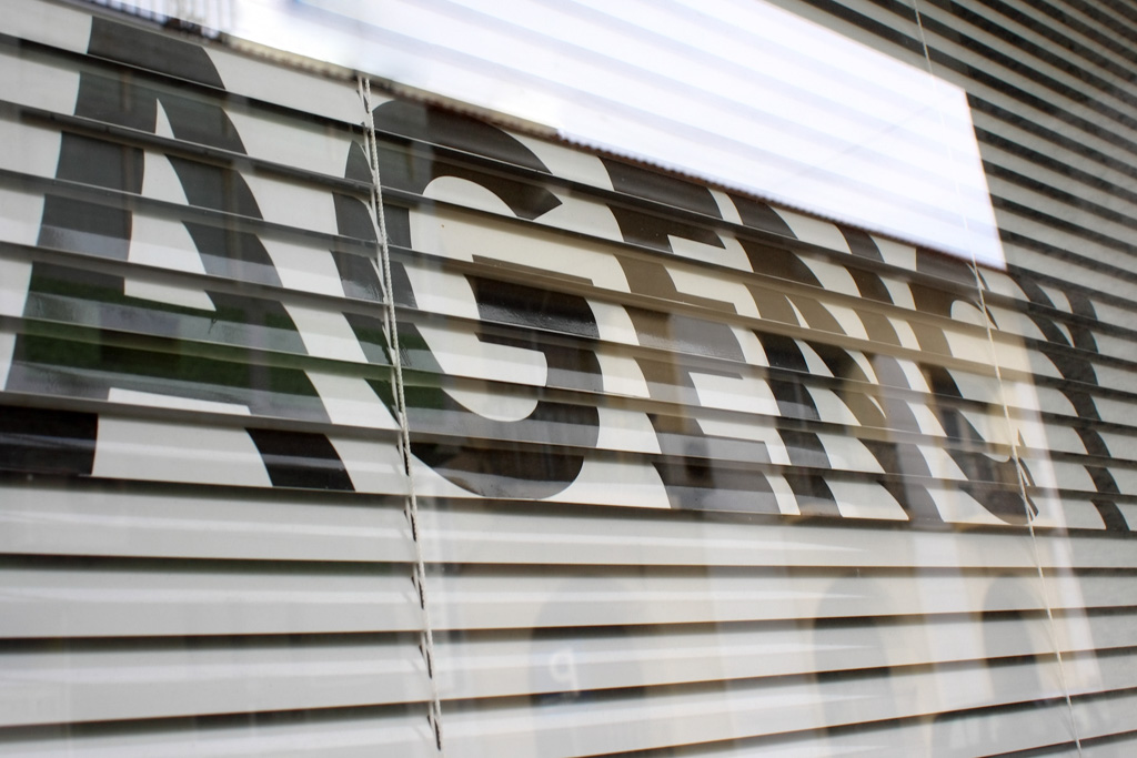 A photo with the word "agency" writing on Venetian blinds.