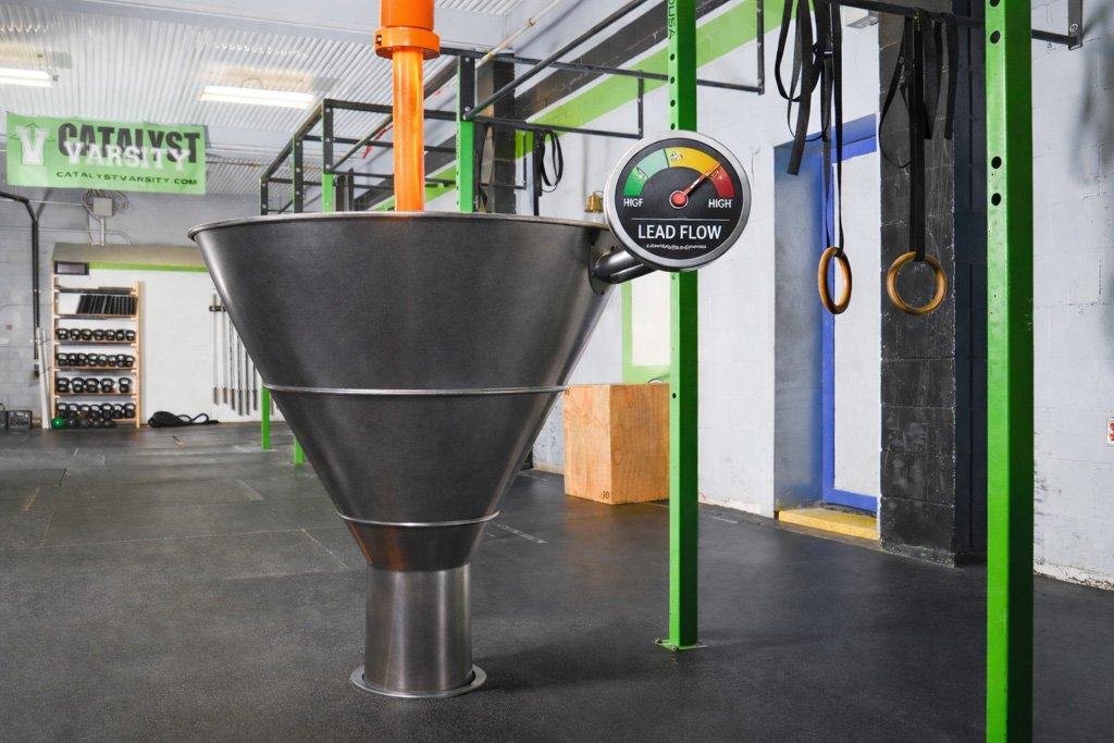 A steady stream of orange liquid flows into a large funnel with a gauge that reads "high lead flow."