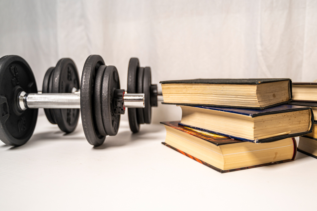A stack of books sits next to two dumbbells.