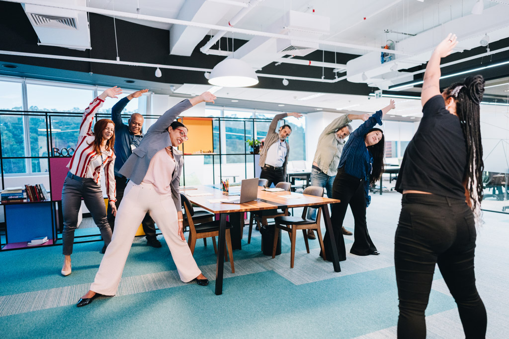 A gym owner leads a stretching seminar in a client's workplace.