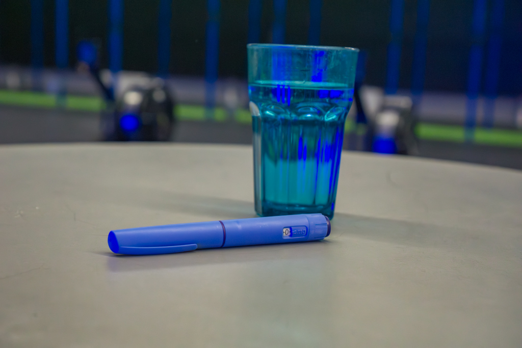 A blue GLP-1 injector pen sits on a desk in a gym.